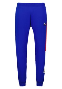 Pantaloni tuta blu con polsini aderenti, caratterizzati da un piccolo logo e dettagli a strisce rosse e bianche sui lati. Realizzati in tessuto morbido per il massimo comfort.