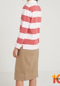 Rood en wit gestreepte lange mouwen polo met een kraag, gecombineerd met een beige rok tot de knie. Het shirt heeft zijsplitten aan de onderrand.