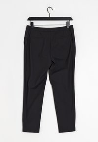 Pantalon noir sur mesure avec une texture lisse, deux poches arrière, coupe slim et une ceinture. Suspendu à un cintre noir sur fond blanc.