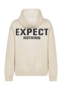 Beiger Kapuzenpullover mit Kordelzughaube, gerippten Bündchen und Saum, mit fettem schwarzem Text auf der Rückseite, der "EXPECT NOTHING." lautet.