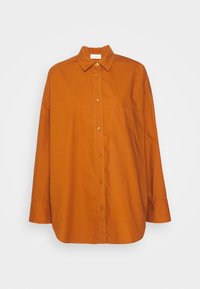Chemise à manches longues orange brûlé avec boutons, col et poche poitrine, présentée sur un fond clair uni.