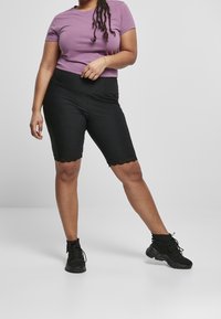Fialové bavlněné tričko, krátké rukávy; černé cyklistické šortky s vlnitým lemem. Černé sportovní boty, texturovaná tkanina a dobře padnoucí design.
