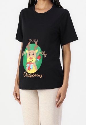 Zwart t-shirt met een cartoonrendier dat een cadeau vasthoudt en de tekst "Have a jolly jolly Christmas", gedragen door een persoon met lichtbeige broek.