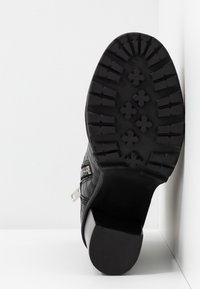 Czarne botki na obcasie z teksturowaną cholewką, gumową podeszwą z bieżnikiem i niskim słupkowym obcasem. Widoczny zamek z boku.