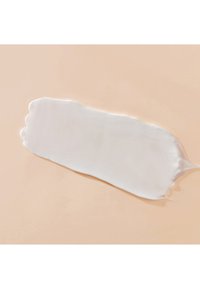 Substance blanche ressemblant à de la crème, en forme allongée et lisse, avec une texture brillante sur un fond couleur pêche.