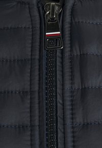 Zbliżenie na zamek błyskawiczny czarnej pikowanej kurtki z metalowym uchwytem z czerwonymi, białymi i czarnymi paskami.