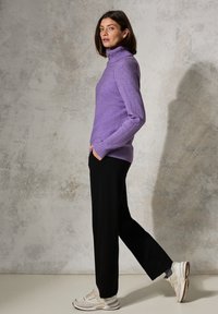Lila, gerippter Rollkragenpullover kombiniert mit schwarzen, locker sitzenden Hosen und beigen Sneakers. Glatte Textur mit Seitentaschen, minimaler Detailierung.