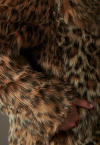 Leopardenmuster-Faux-Fur-Stoff mit langen, weichen Fasern in Brauntönen, Schwarz und Beige, der eine strukturierte, plüschige Optik aufweist.