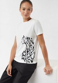 White t-shirt featuring a black tiger graphic and abstract pattern design. Short sleeves and a round neckline, made of smooth fabric.
