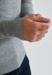Pull gris à côtes avec des poignets ajustés. Le matériau semble doux et texturé, avec un design sans coutures et un ourlet droit.