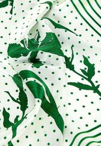 Groene bloemenprint op witte zijden stof met stippen en golvende lijnpatronen, gladde textuur en levendig kleurcontrast.