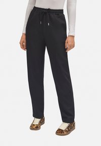 Pantalones jogger negros con una cinturilla texturizada y cordón, de corte relajado. Combinados con zapatillas de leopardo en tonos marrón y negro.