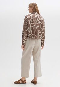 Cropped brown shirt with white abstract pattern, paired with light-colored, loose-fitting trousers and brown strappy sandals.