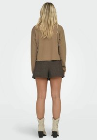 Brązowy sweter z prążkowanym wzorem, krótki, z długimi rękawami, zestawiony z szarymi szortami. Model ma na sobie beżowe botki kostkę z czarnymi obcasami. Widok z tyłu.
