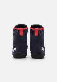 Navy blue climbing shoes with mesh detailing, red accents, and a textured rubber sole. Features a logo on the heel and pull tab for easy wear.