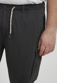 Kohlgraue Hose aus gewebtem Stoff, mit elastischem Bund und Kordelzug, seitlicher Tasche und Knopfdetails.