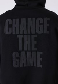 Sweat à capuche noir avec de grandes lettres gris foncé dans le dos indiquant "CHANGE THE GAME" en trois lignes.