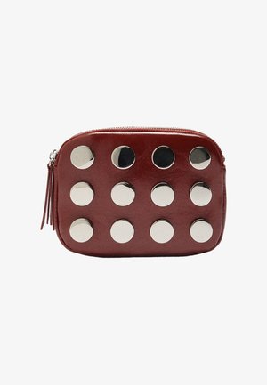 Czerwona skórzana sakiewka z metalowymi srebrnymi okrągłymi ćwiekami ułożonymi w rzędach, z zamknięciem na zamek błyskawiczny i ozdobnym frędzlem po boku.
