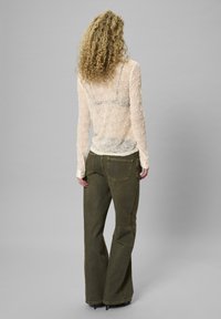 Durchsichtige, strukturierte Creme-Bluse mit langen Ärmeln, kombiniert mit olivegrünen, hochtaillierten, weiten Hosen, die über Rückentaschen und eine lockere Passform verfügen.
