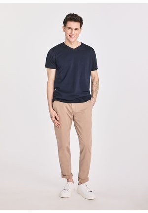 Granatowy T-shirt z dekoltem w serek w połączeniu z beżowymi chinosami i białymi sneakersami. Charakteryzuje się dopasowanym krojem i miękką, gładką fakturą. Prosty i casualowy.