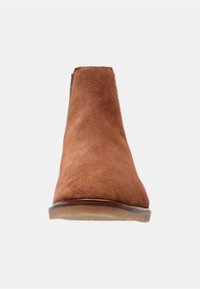 Bottine en suede marron avec une texture lisse, bout arrondi et petit talon. Design simple avec des coutures minimalistes et aucun élément métallique visible.