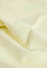 Měkká, texturovaná bavlněná tkanina v bledě žluté barvě, s jemným žebrováním a hladkým splýváním, vytvářejícími jemné záhyby a sklady.