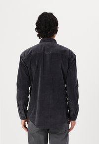 Camicia in velluto a coste slim-fit grigia scura con colletto button-down, maniche lunghe e orlo curvo. Presenta una texture a coste verticali.