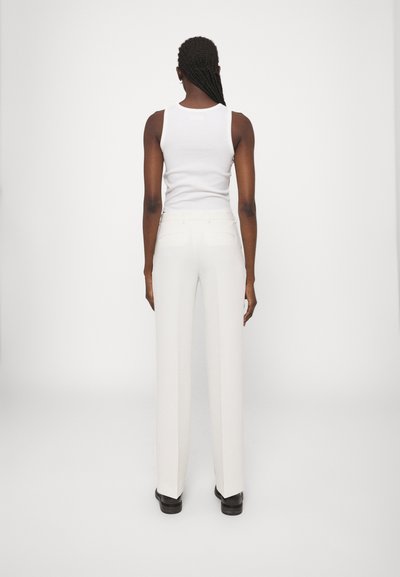 Pantalons larges blancs en tissu lisse, avec des poches arrières et une taille simple, associés à un débardeur blanc ajusté.