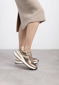 Zapatillas deportivas en oro rosa con acentos de estampado de leopardo, detalles de malla, cierre con cordones y una suela blanca acolchada.