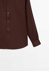 Chemise marron foncé à manches longues avec boutons sur le devant et poignet à bouton unique, présentée sur fond blanc.