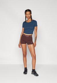 Marineblå, kort t-skjorte med korte ermer, kombinert med brune Nike Pro-sportshorts med kontrastliv. Sorte joggesko fullfører antrekket.