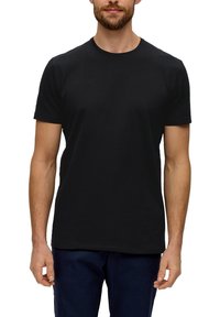 Camiseta negra de manga corta de algodón con cuello redondo, diseño liso y corte relajado. Combinada con pantalones de mezclilla oscuros.
