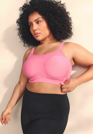 Pink sports bra with structured cups, adjustable straps, and front seam detailing. Paired with high-waisted black leggings.