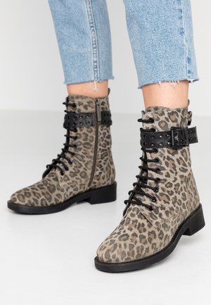 Des bottines à imprimé léopard en tissu doux présentent des clous ronds noirs et une sangle à boucle, lacées à l'avant avec un talon empilé bas.