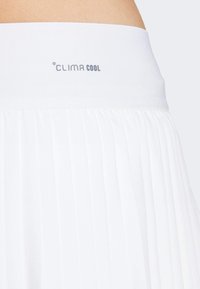Hvit plissert skjørt laget av et mykt materiale. Har en bred elastisk midje med "CLIMA COOL" merke i grått. Teksturert lett materiale.