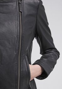 Black leather jacket with a fitted design, featuring a silver zipper closure, side pocket, and smooth texture. Minimalist style details visible.
