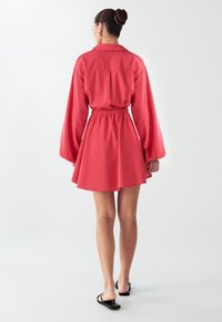 Rotes Kleid mit einer taillierten Taille und Ballonärmeln. Hergestellt aus einem leichten Stoff, mit einem Kragen und einem ausgestellten Saum.