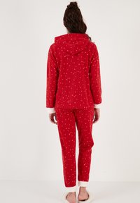 Röd pyjamasset med huva, ribbat material, prydd med små vita prickar, och matchande byxor med vita fluffiga muddar.