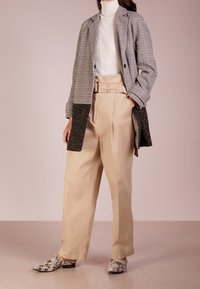 Ternet blazer med kontrastpanel i leopardprint, cremefarvet rullekrave, beige plisserede bukser og mønstrede slip-on sko. Glatte teksturer over det hele.