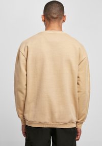 Sudadera beige con cuello redondo, corte relajado y puños y dobladillo acanalados. Textura suave, diseño minimalista, sin patrones o acentos visibles.
