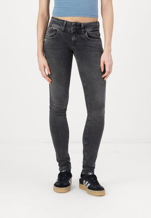 Slim fit sorte jeans båret af en stående person kombineret med sorte og hvide sneakers og en blå cropped top.
