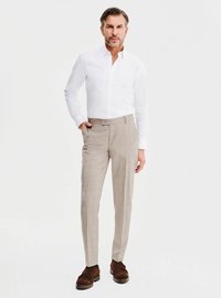 Biała koszula zapinana na guziki w połączeniu z jasnobeżowymi spodniami w kratę i brązowymi zamszowymi butami. Model stoi z jedną ręką w kieszeni.