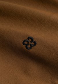 Tissu brun foncé avec un petit motif noir brodé de quatre boucles reliées au centre.