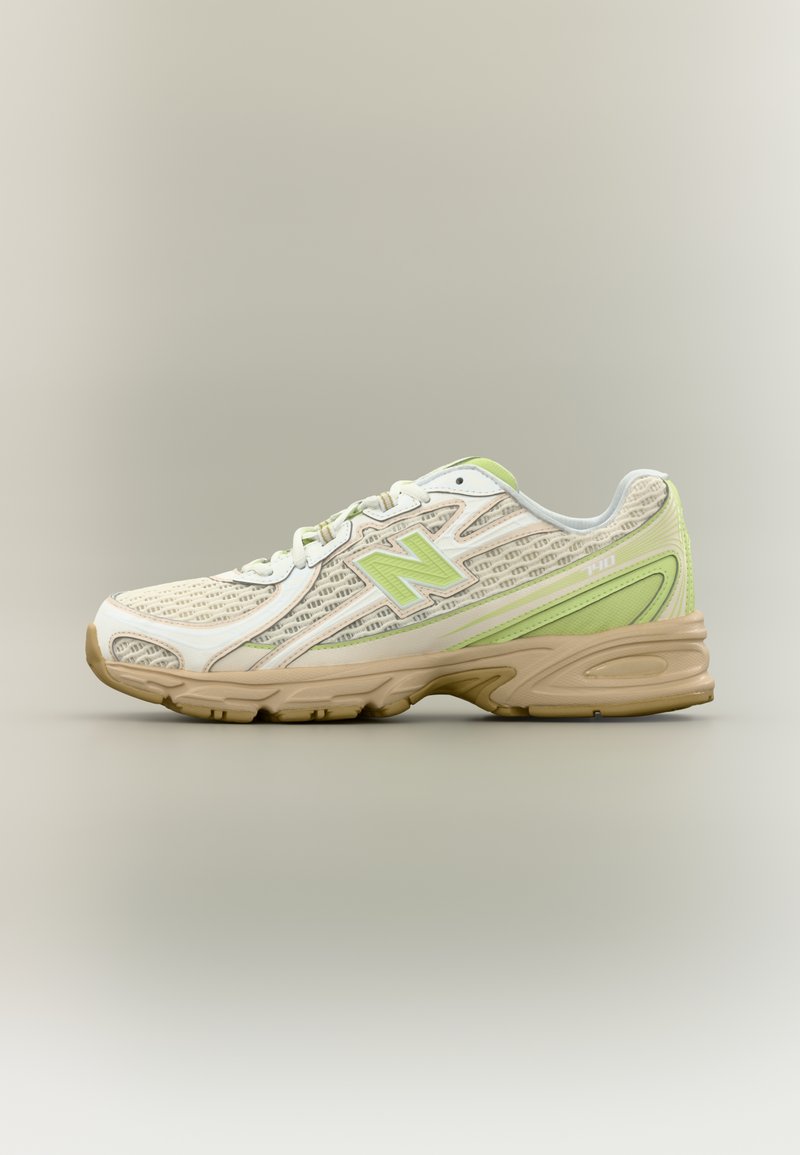 Παπούτσι New Balance σε μπεζ και ανοιχτό πράσινο, με υφή από δίχτυ, σχεδιασμό με κορδόνια και ταμπά καουτσούκ σόλα, εμφανιζόμενο σε πλευρικό προφίλ σε ουδέτερο φόντο.