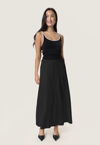 Zwarte maxi rok met een gestrikt taille, gecombineerd met een zwart tanktop met witte accenten. Glad materiaal, eenvoudig ontwerp en tot de enkels.