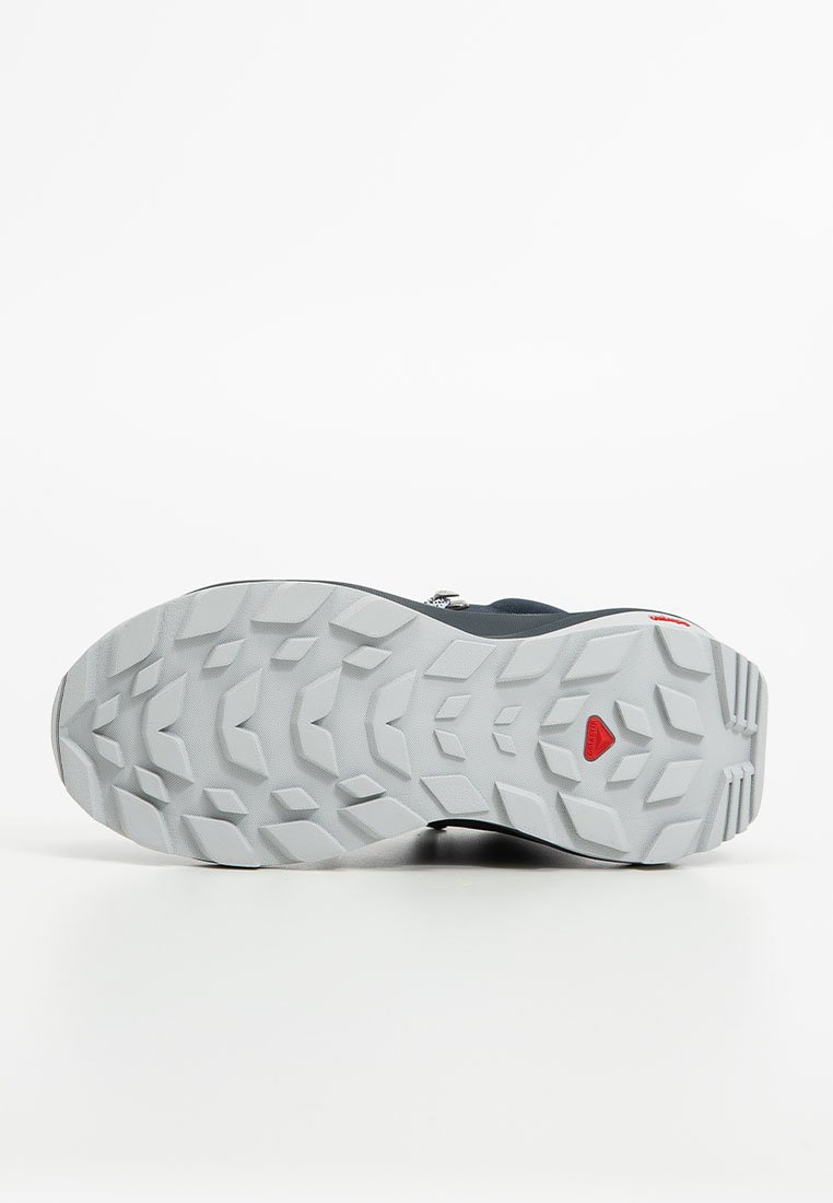 Schuhsohle aus grauem Gummi mit tiefen Traktionsmustern und einem roten Akzent; entworfen für Langlebigkeit und Grip auf verschiedenen Oberflächen.