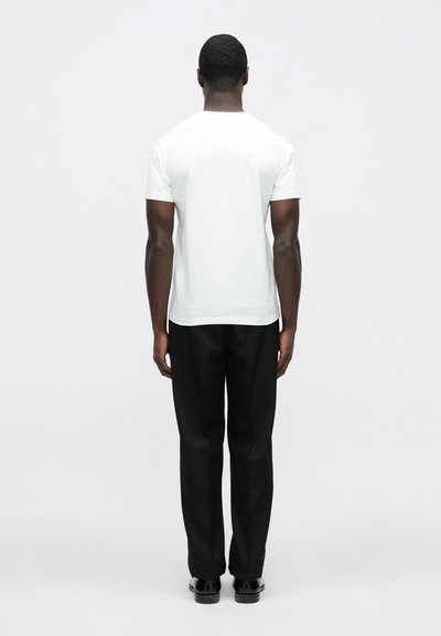 Biała koszulka z krótkim rękawem i okrągłym dekoltem, zestawiona z czarnymi, dopasowanymi spodniami, widziana od tyłu na jednolitym tle.