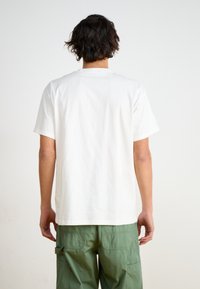 White cotton T-shirt with short sleeves, straight cut, and a crew neck. Pairing with green cargo pants visible at the waist.
