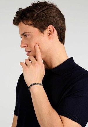 Bracciale argento con accenti rettangolari blu e neri alternati. Indossato su una mano di carnagione chiara, in un'inquadratura ravvicinata di profilo.