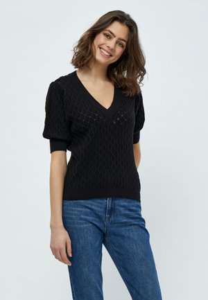 Maglione nero a maniche corte lavorato a maglia con scollo a V, caratterizzato da un motivo testurizzato e orlo a coste. Abbinato a jeans in denim blu.